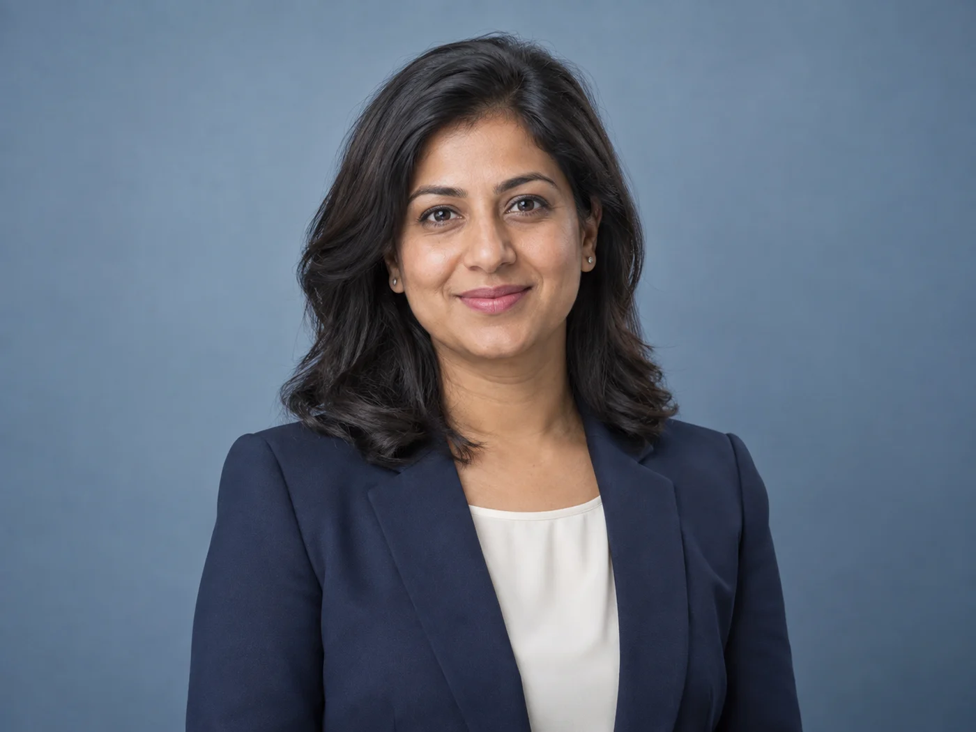 Illustrative professional headshot with natural skin texture, a navy blazer and a soft studio background.